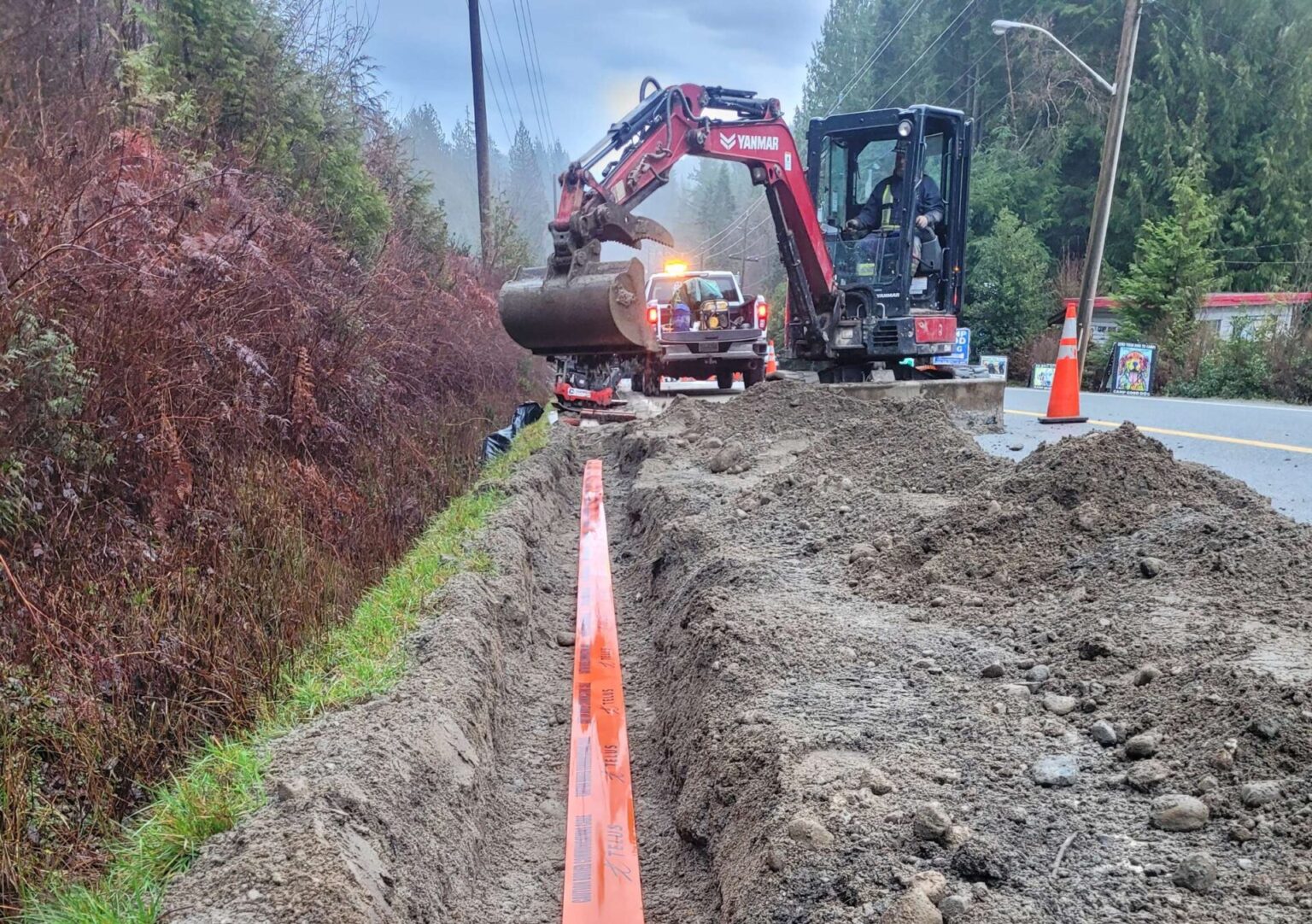 Mini excavator trenching beside a road with orange conduit laid in the trench